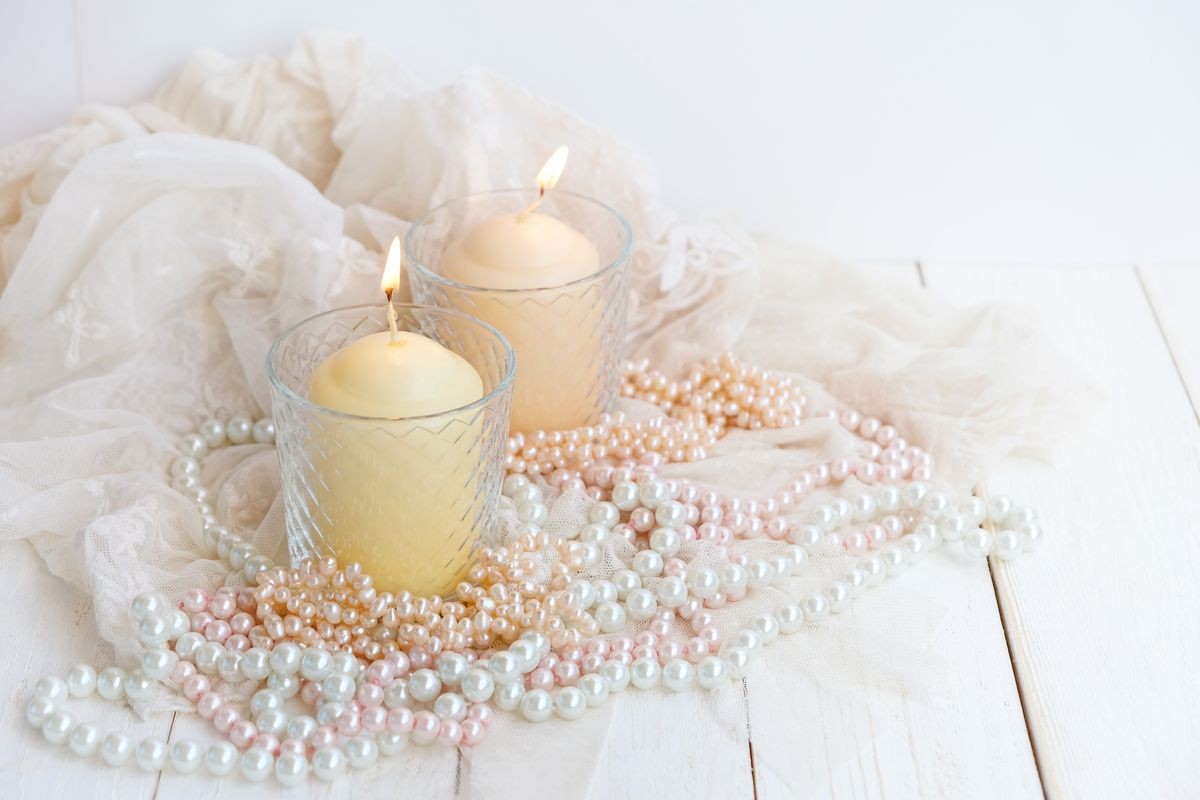 still life with burning candles and pearls beads on white wooden table close up. romantic elegant gentle composition in women's boudoir. vintage style